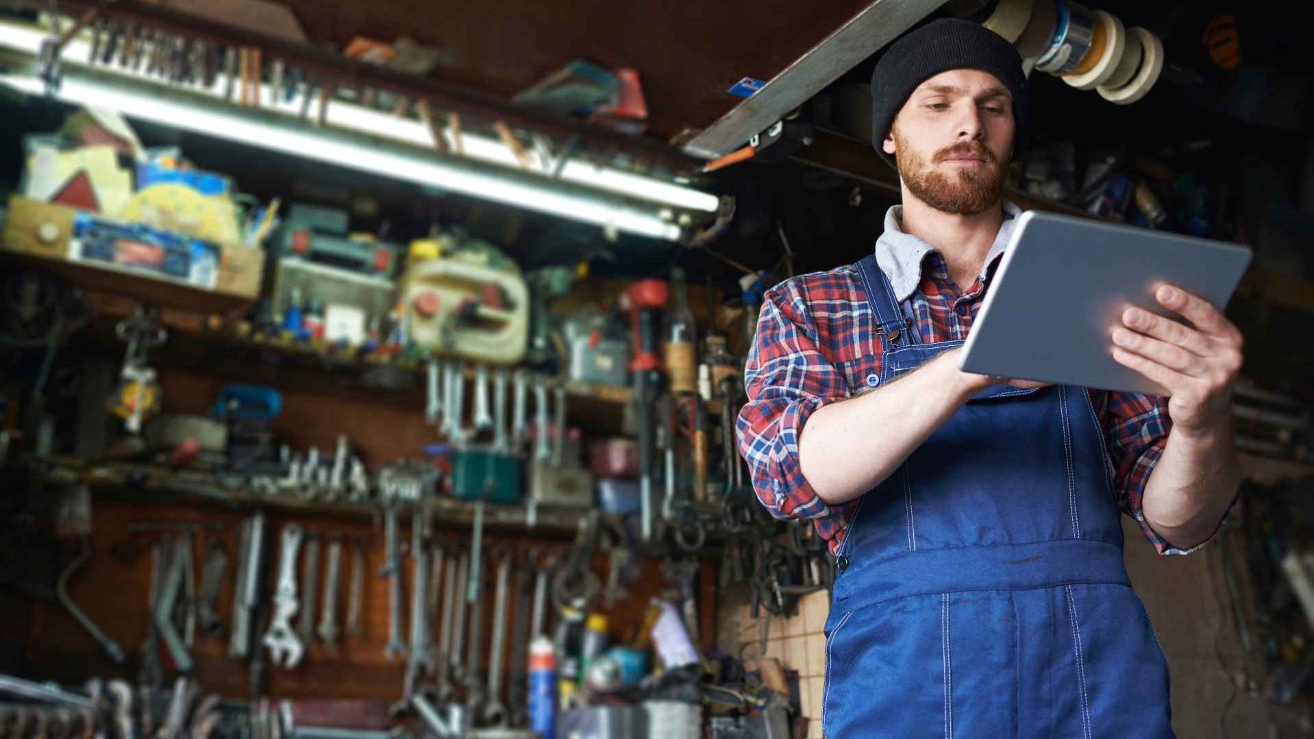 Low angle portrait of handsome mechanic using tablet to check auto systems in repair workshop